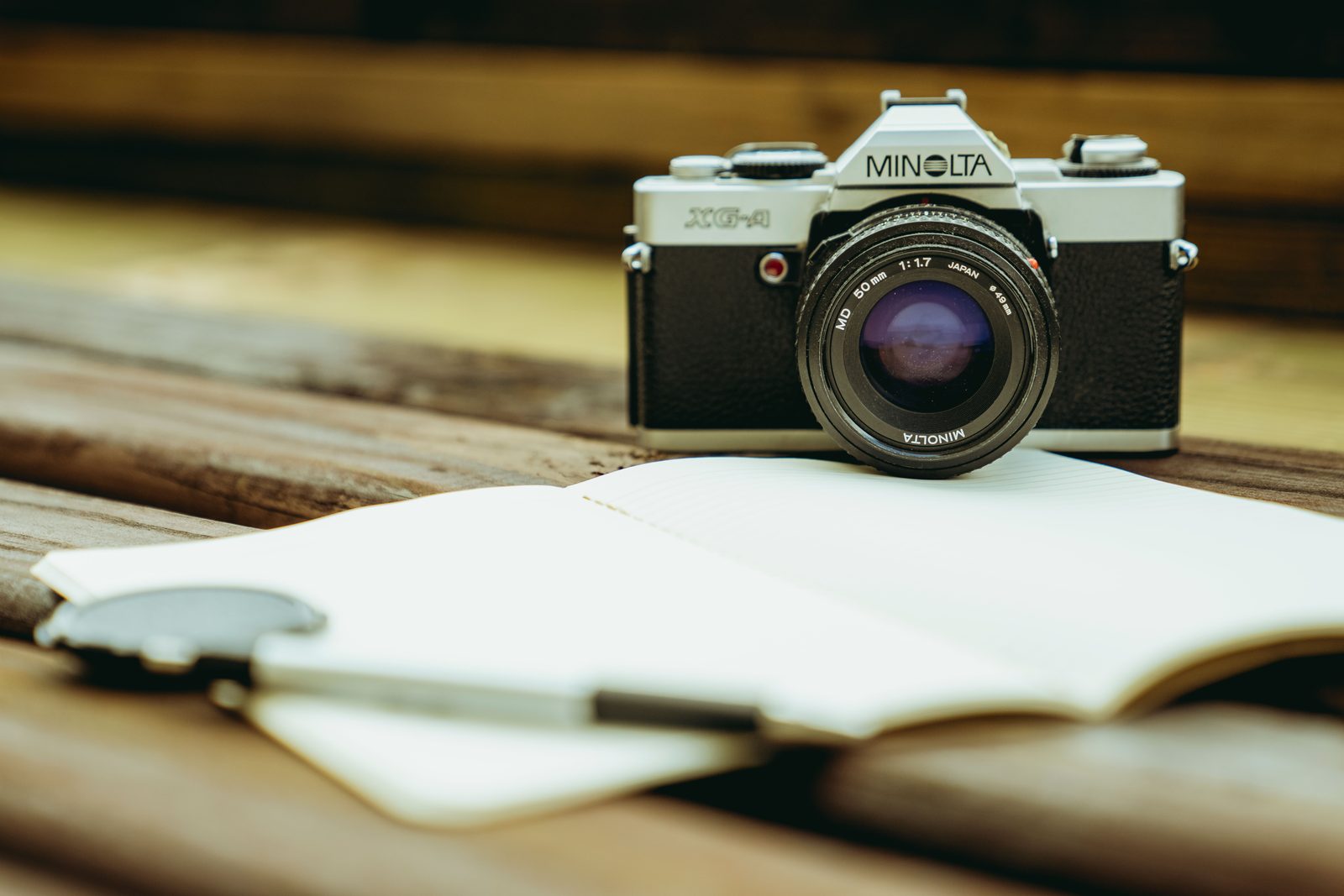 Een fotocamera op een houten tafel naast een opengeslagen notitieboek met een pen