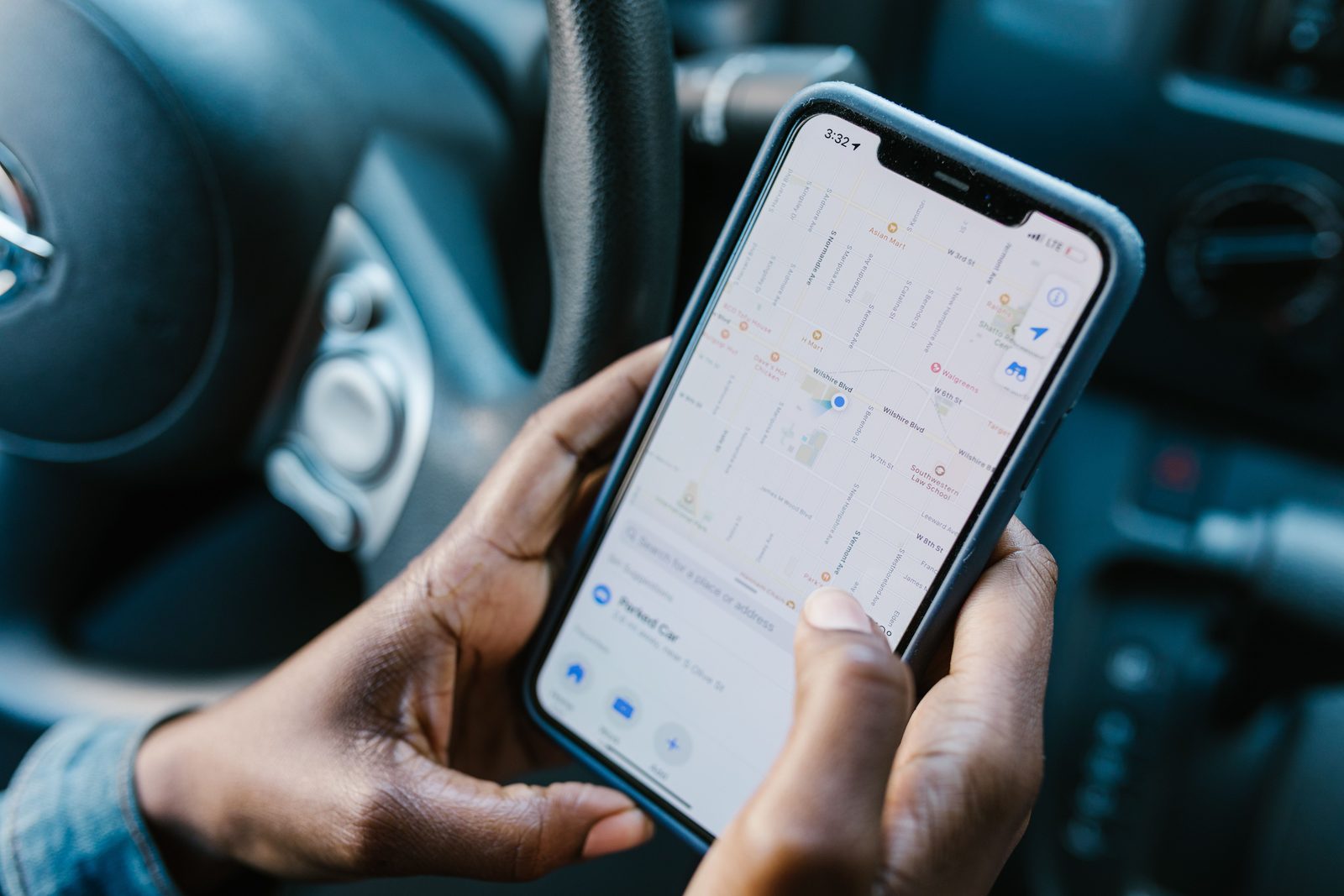 Een hand met een telefoon waarop een kaart van de omgeving staat, achter het stuur van een auto