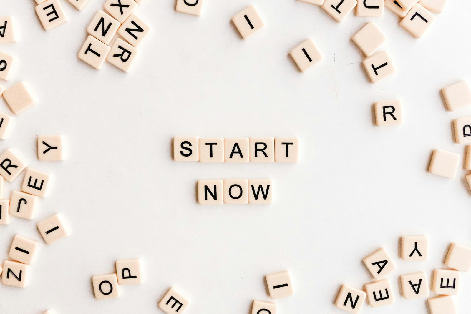 Verspreide lettertegels op een witte ondergrond met in het midden de woorden start now, symbool voor het kiezen van zoekwoorden